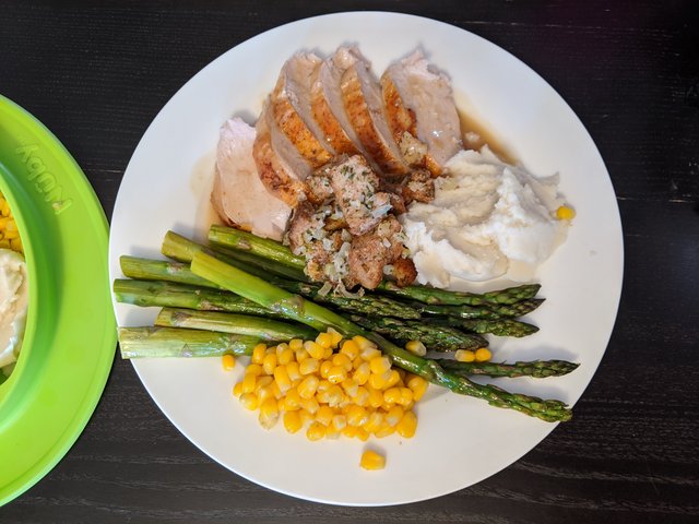 Plated turkey slices with mashed potatoes, roasted asparagus, stuffing, and corn